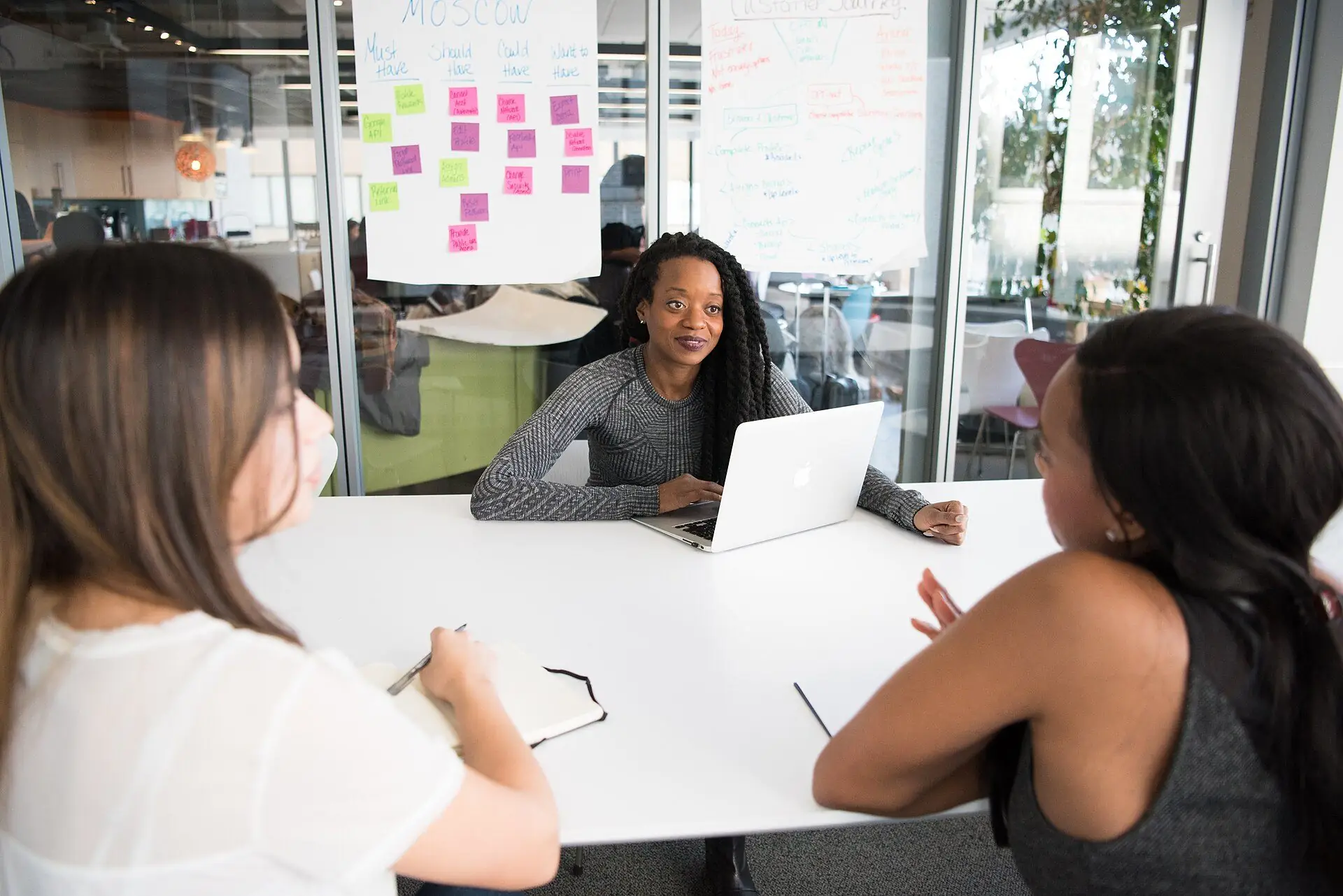 Equipe reunida em mesa de escritório planejando com um quadro de post-its ao fundo